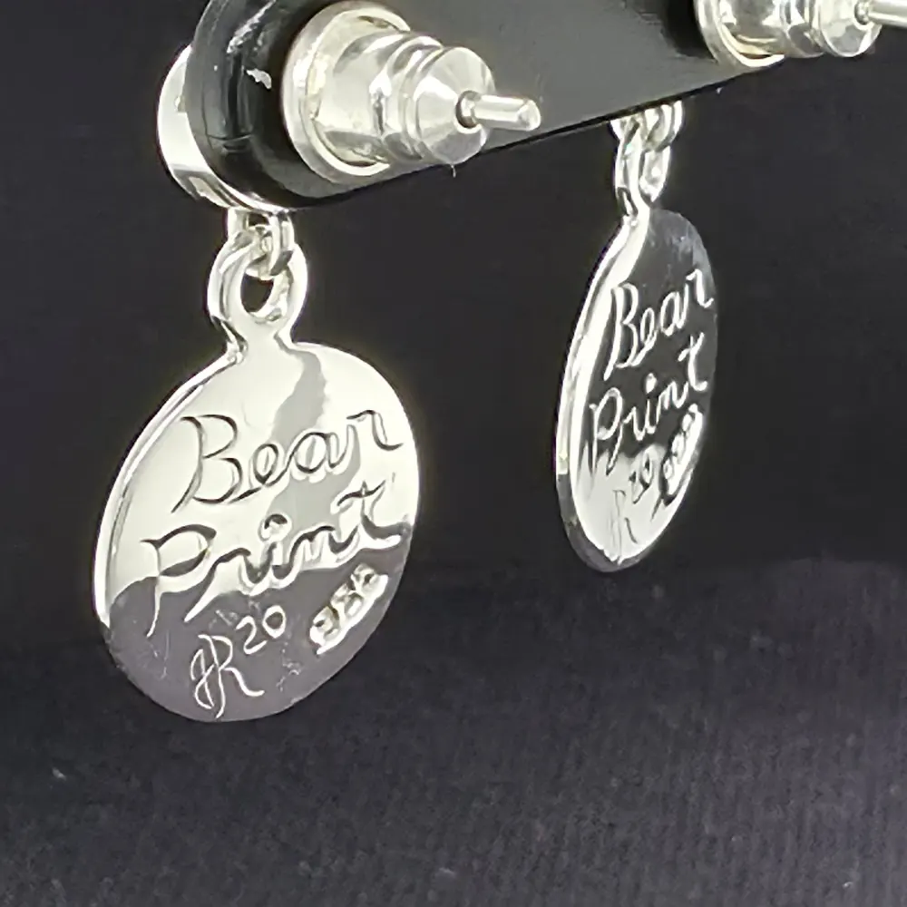 Back detail of the bear print earrings against dark textured material