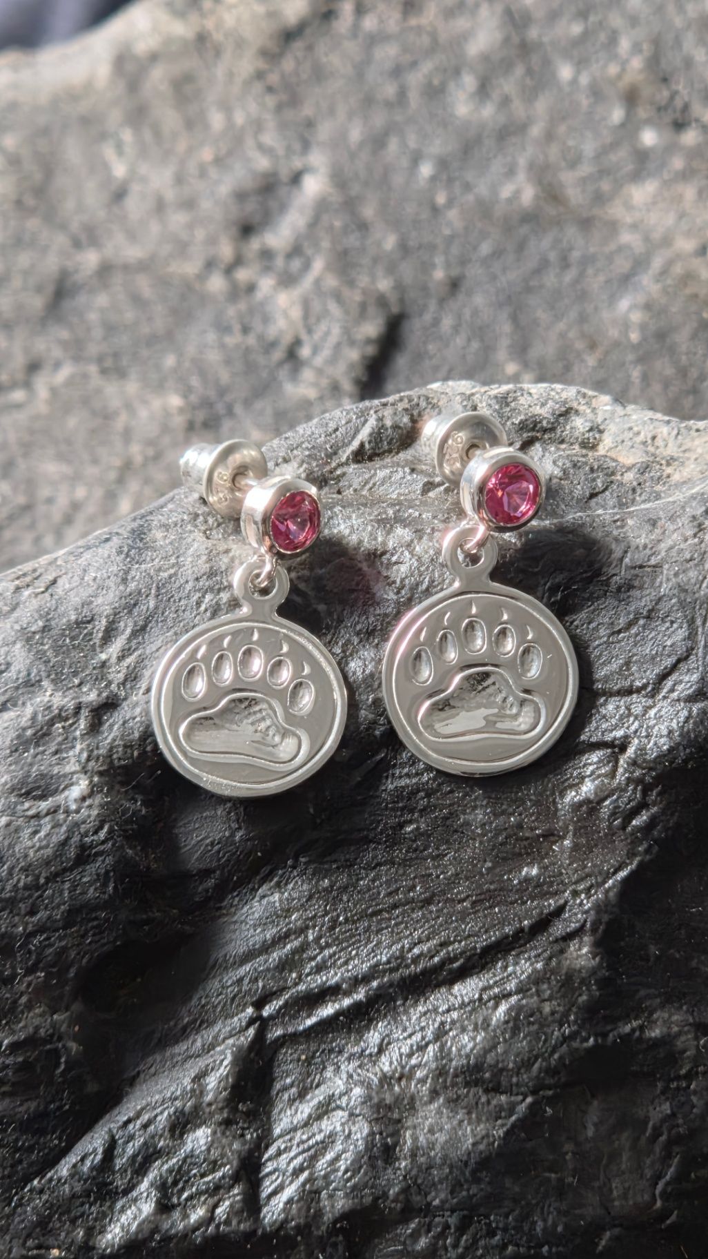 Sterling silver bear print earrings resting on a textured rock